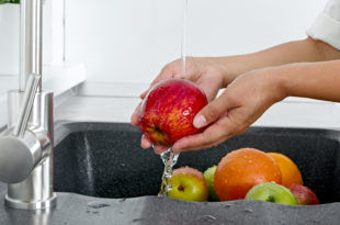 Cook woman washes an apple under running water from a water tap.