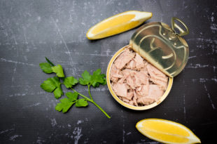 Canned tuna with lemon and parsley on dark background, top view.