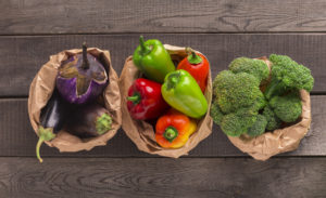 Tre sacchetti di carta con verdura fresca; da sinistra a destra: melanzane, peperoni rossi e verdi, broccoli; concept: verdura biologica