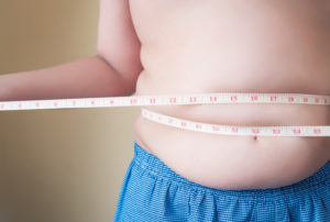 Primo piano della pancia di un bambino in sovrappeso a torso nudo, con metro a nastro avvolto intorno alla vita