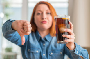 Redhead woman holding soda refreshment with angry face, negative sign showing dislike with thumbs down, rejection concept sugar tax