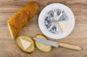 Piatto con formaggini confezionati, accanto a fette di pane con formaggino e coltello per spalmare