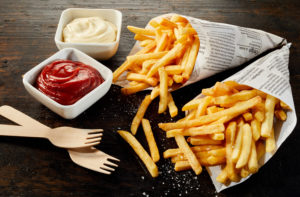 Patatine fritte in coni di carta di giornale con ketchup e maionese e forchettine compostabili per takeaway o food delivery