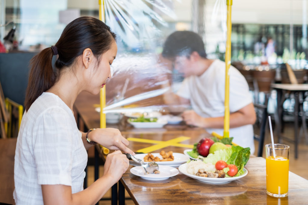 Asian couple man and woman sitting in restaurant eating food with table shield to protect infection from coronavirus covid-19, restaurant and social distancing concept