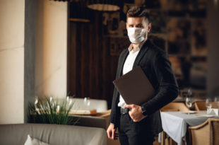 Handsome adult bearded man indoors in cafe. Lifestyle concept photo with copy space. Picture with gray laptop and protective mask on the face