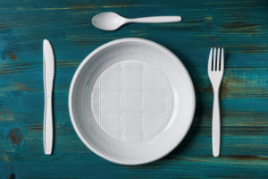 piatto, forchetta, coltello e cucchiaio in plastica monouso bianca su ripiano color petrolio