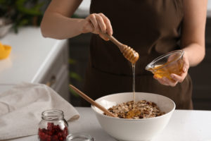 Donna versa miele in una ciotola per fare una granola o un muesli