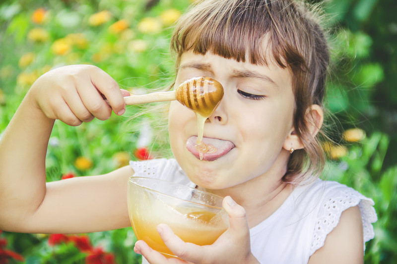 Bambina che si fa colare il miele sulla lingua con l'apposito attrezzo di legno