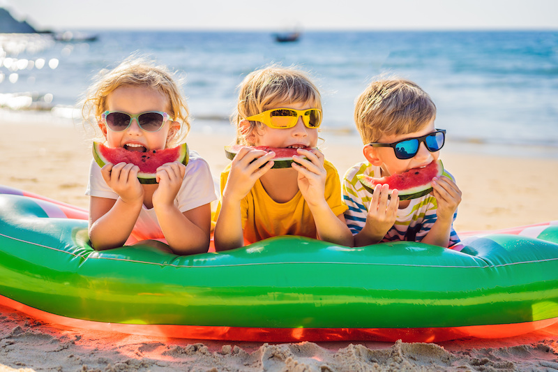 Tre bambini sulla spiaggia, mangiano una fetta d'anguria indossando occhiali da sole, concept: sicurezza alimentare