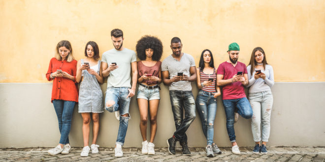 Multiracial friends using smartphone against wall at university college backyard - Young people addicted by mobile smart phone - Technology concept with always connected millennials - Filter image
