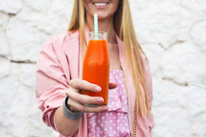 Giovane donna tiene in mano bottiglietta di vetro co succo di frutta o bevanda zuccherata con cannuccia; concept: bibite, smoothies