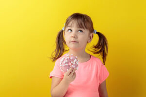 merenda Bambina pensierosa con una ciambella glassata o donut in mano; concept: bambini, dolci, merendine