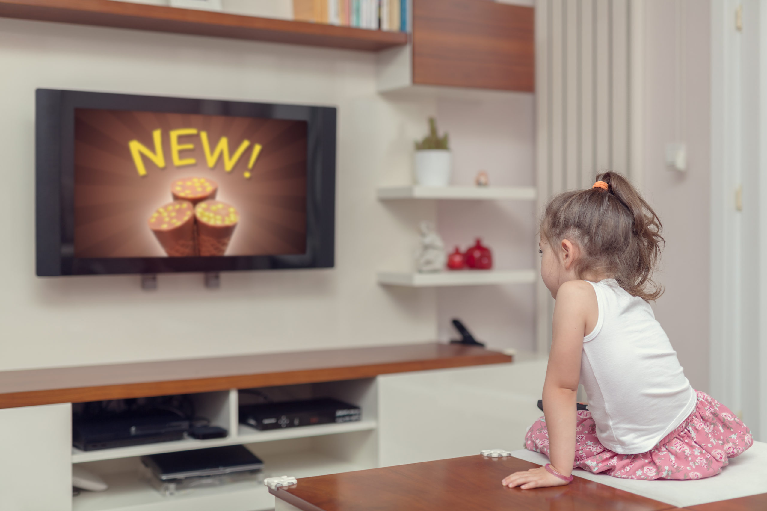 Bambina seduta su un tavolino davanti alla televisione guarda una pubblicità di un prodotto alimentare