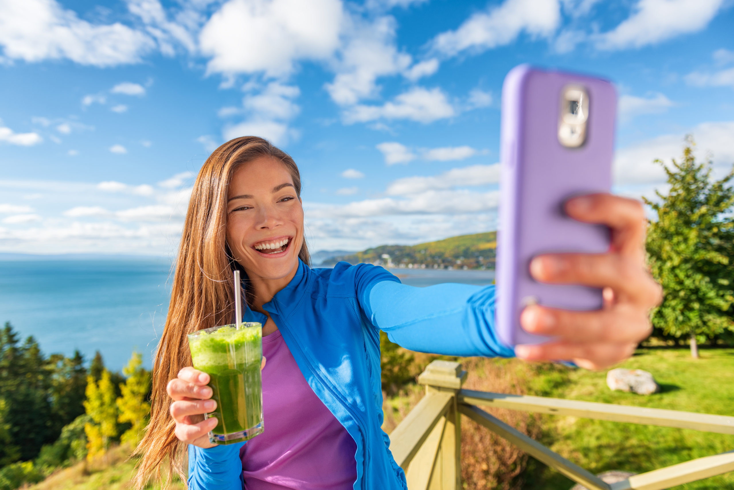 Ragazza si fa un selfie con lo smartphone all'aperto con uno smoothie