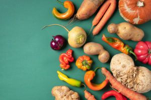 Trendy ugly organic vegetables. Assortment of fresh eggplant, onion, carrot, zucchini, potatoes, pumpkin, pepper in craft paper bag over green background. Top view. Cooking ugly food concept. Non gmo vegetables