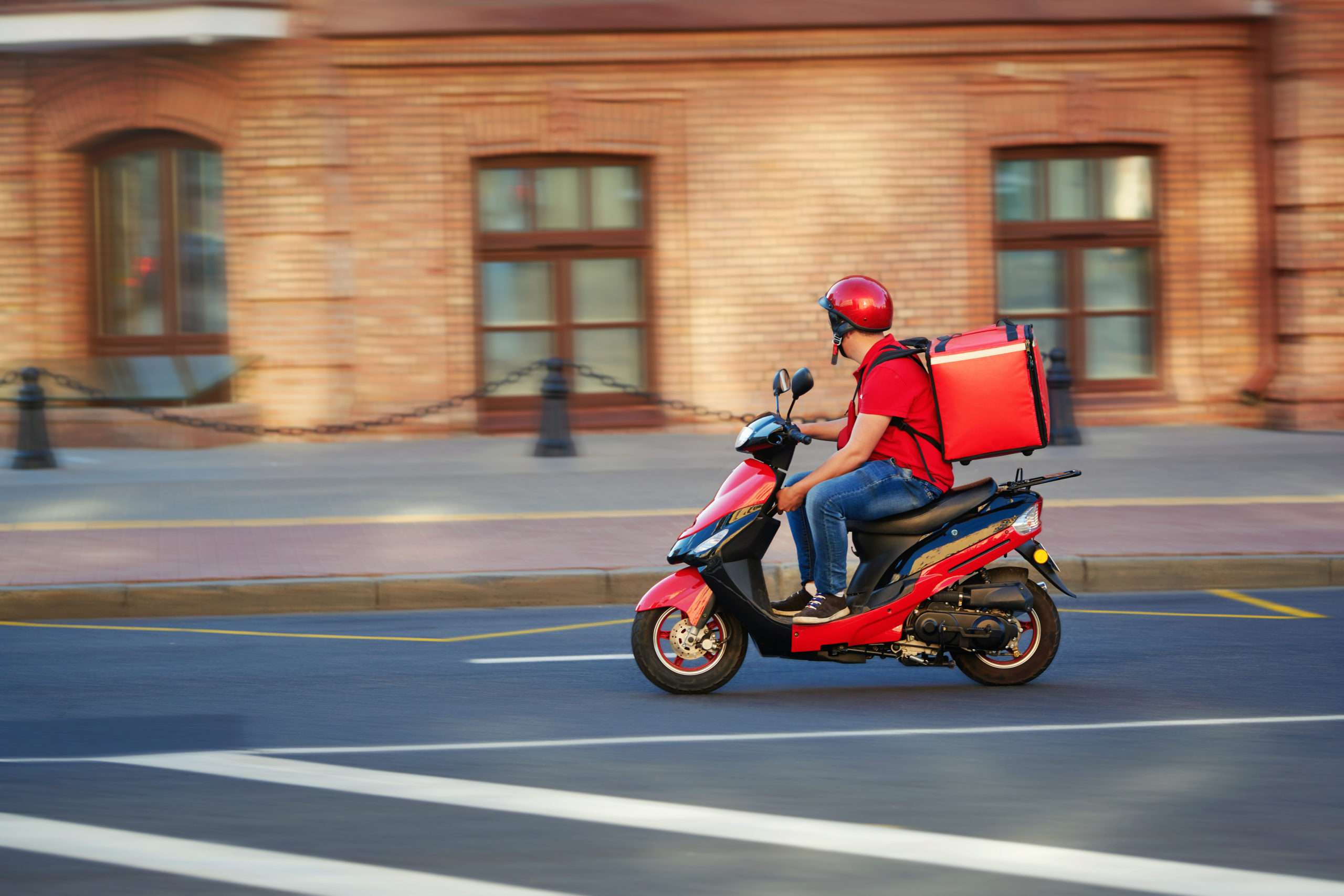 Un fattorino del food delivery con zaino termico su un motorino per strada