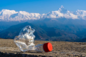 Bottiglia di plastica schiacciata a terra, con montagne sullo sfondo; concept: inquinamento, riciclo, vuoto a rendere, deposito cauzionale