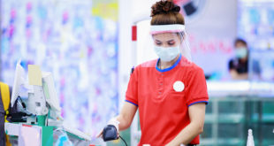 female supermarket cashier in medical protective mask and face shield working at supermarket