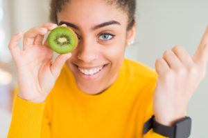 alimentazione salute dieta donna frutta kiwi veg Young african american girl eating green kiwi very happy pointing with hand and finger to the side
