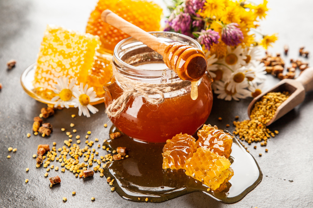 Vasetto di miele, con pezzi di favo, polline e fiori