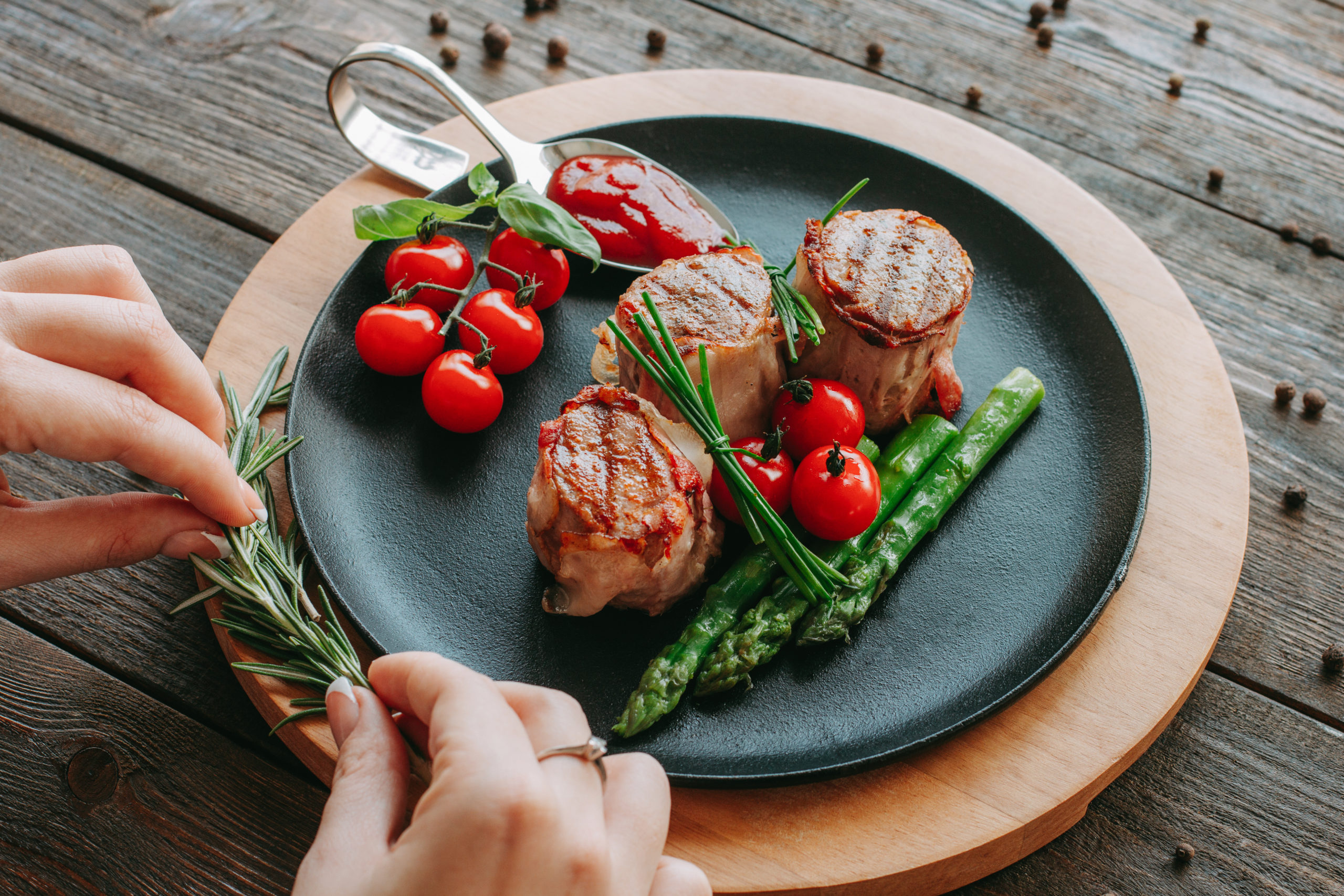 Carne, medaglioni in piatto nero con asparagi, pomodorini, salsa rubra e rosmarino