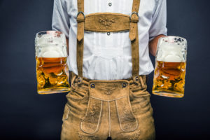 Uomo con abiti tipici bavaresi tiene due boccali di birra; concept: oktoberfest