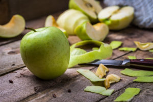 Mela verde su un tavolo di legno circondata da bucce di mela