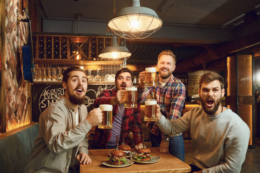 Un gruppo di uomini brinda con boccali di birra in un pub guardando un evento sportivo