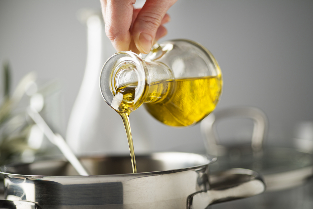 Persona versa olio extravergine di oliva in una pentola in cucina