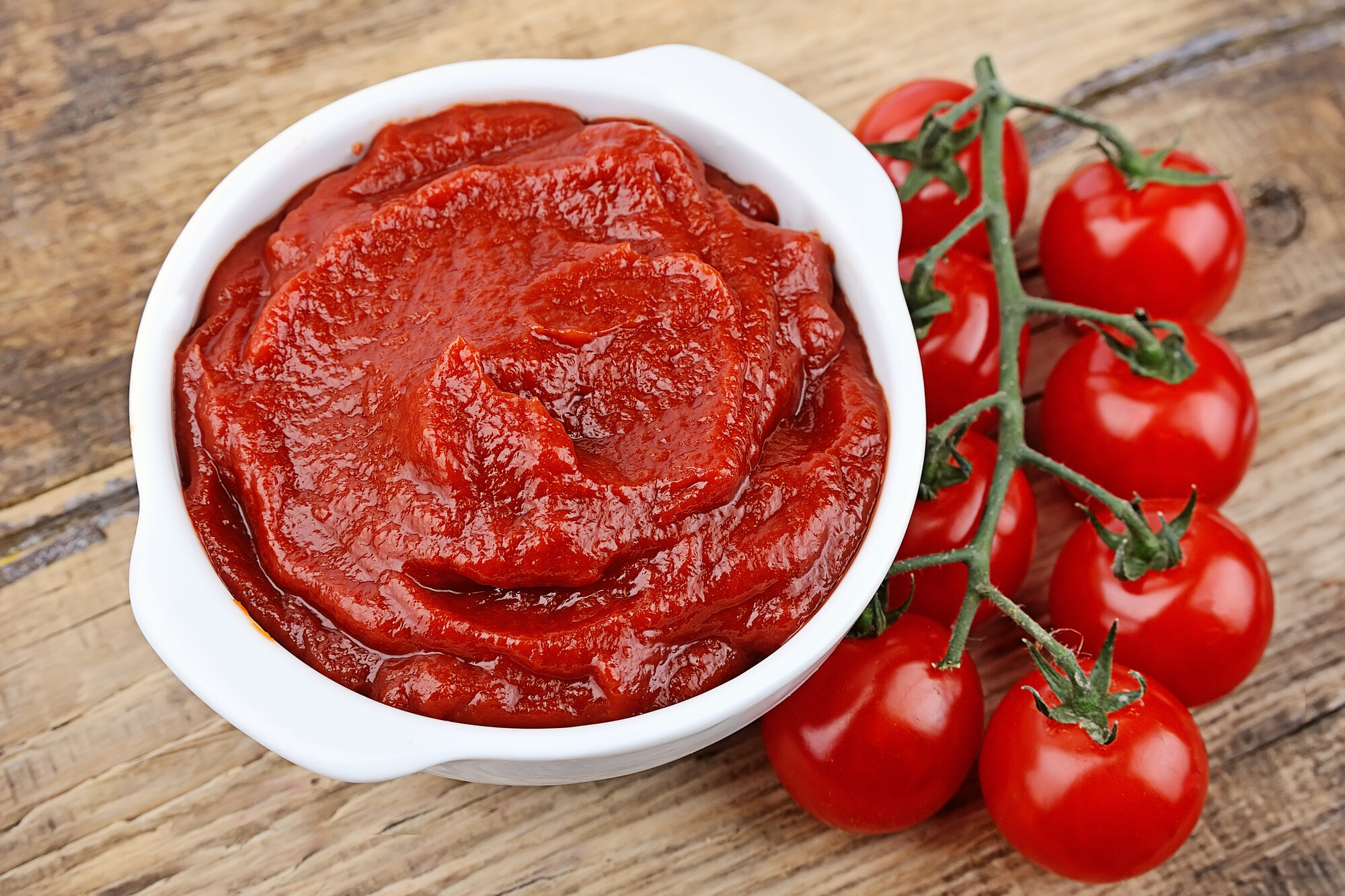 concentrato di pomodoro in ciotola bianca su tavolo di legno con pomodorini a grappolo