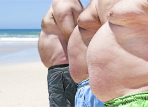 Tre uomini in sovrappeso in costume sulla spiaggia; concept sovrappeso, obesità