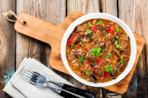 Piatto di stufato di carne di manzo con funghi e paprika su un tagliere accanto a posate