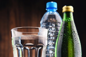 Acqua minerale in bottiglie di plastica e vetro e in bicchiere