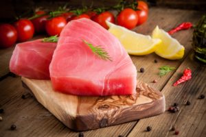 Filetti di tonno a fette su un tagliere di legno, sullo sfondo pomodorini, limone e peperoncini