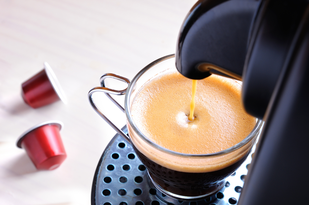 Caffè espresso da macchinetta nella tazzina, con capsule per caffè sullo sfondo