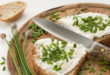 Pane con formaggio spalmabile e erba cipollina su tagliere con coltello