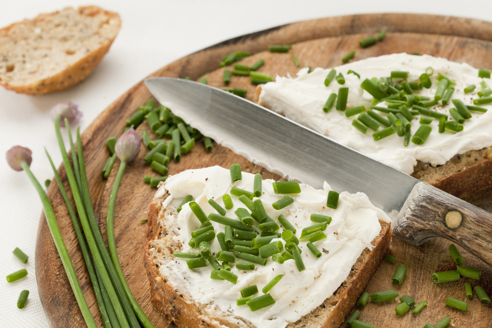 Pane con formaggio spalmabile e erba cipollina su tagliere con coltello