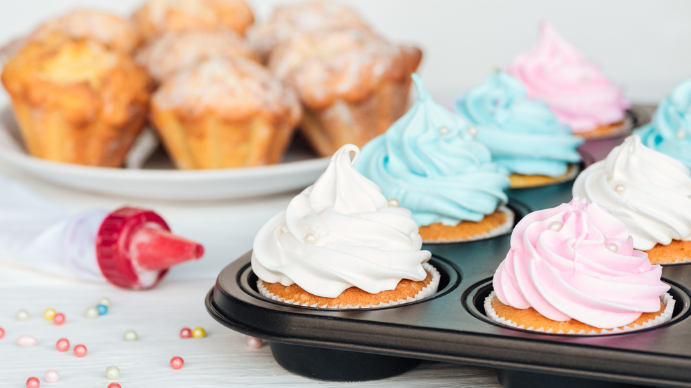 Cupcake con glassa colorata in una teglia da muffin, sullo sfondo altri cupcake da decorare