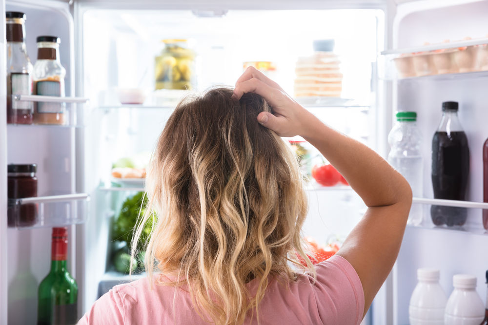 Donna confusa osserva frigorifero aperto; concept sicurezza alimentare