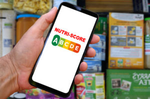 nutri-score sullo schermo di uno smartphone tenuto davanti a un assortimento di prodotti