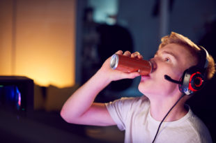 Ragazzo adolescente beve bevanda zuccherata o energy drink mentre gioca con i videogiochi