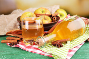 aceto di mele in bottiglia rovesciata con bicchiere pieno, cestino di mele, stecche di cannella e una bacca di anice stellata