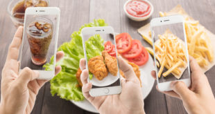 Tre smartphone inquadrano, da sinistra a destra, bicchiere di bibita gassata, pollo fritto e patatine fritte; concept junk food e influencer