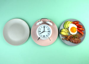 Tre piatti: a sinistra vuoto, al centro con una sveglia, a destra pieno di cibo; concept: digiuno intermittente