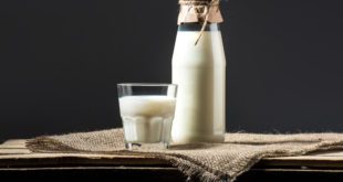Bicchiere di latte e bottiglia di latte chiusa con carta e spago, appoggiati su tovaglietta di yuta su un tavolo