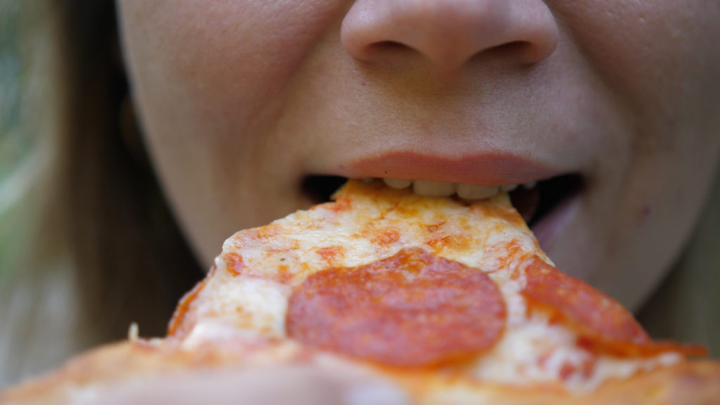 Young woman outdoors eating italian pizza. Close up bites a piece of pizza