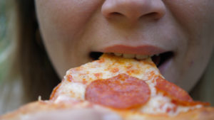 Giovane donna all'aperto che mangia pizza italiana. ragazza morde un pezzo di pizza, salame