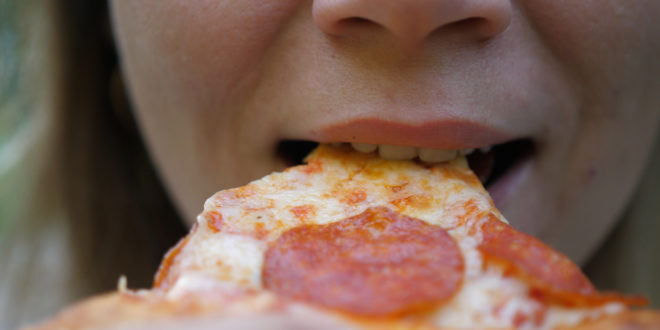 Young woman outdoors eating italian pizza. Close up bites a piece of pizza