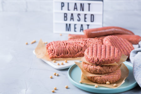 Sostituti vegetali tipo burger, salsicce e trita, con cartello sullo sfondo “plant based meat”