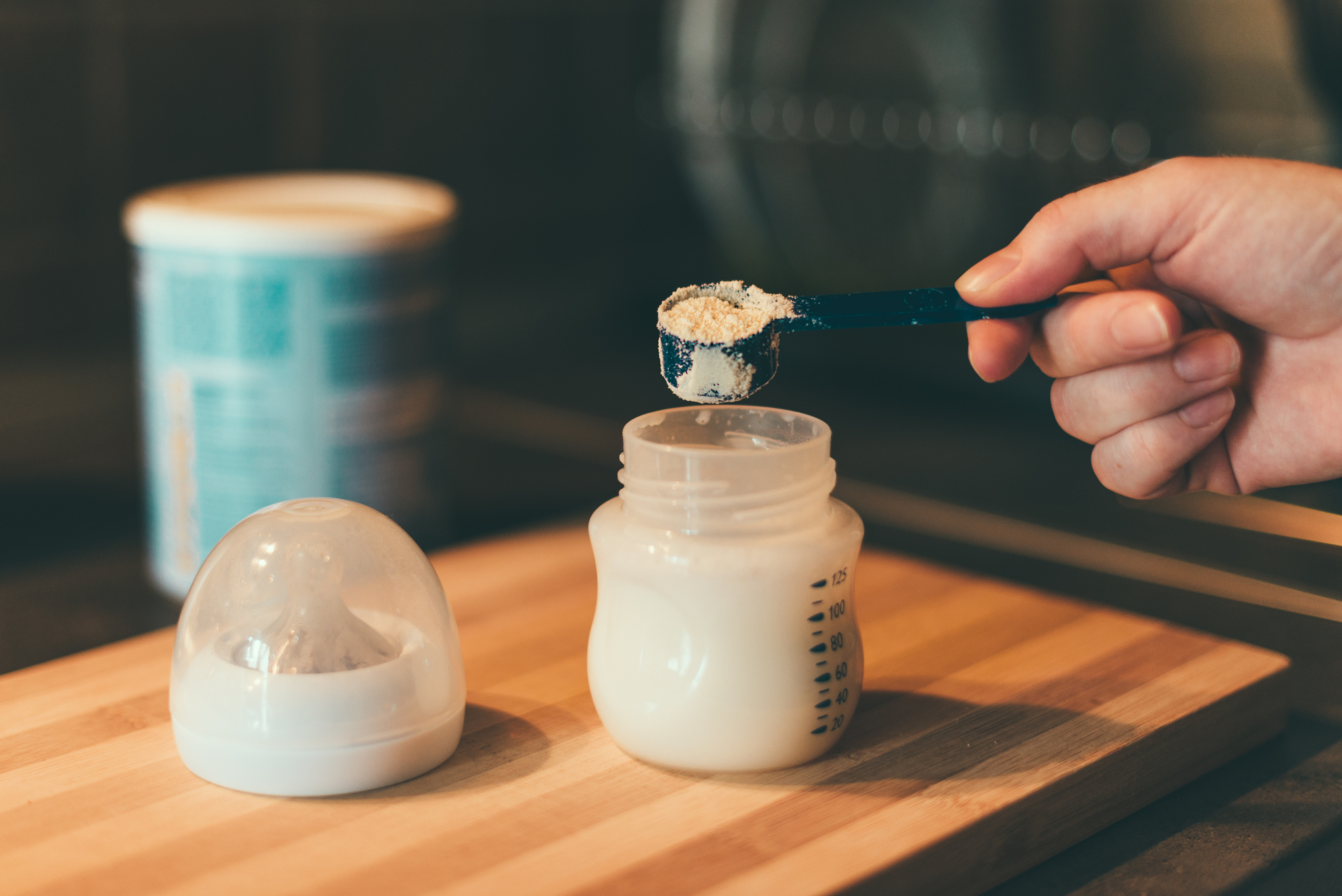 Una persona versa latte artificiale o latte in polvere in un biberon con un misurino, sullo sfondo latta